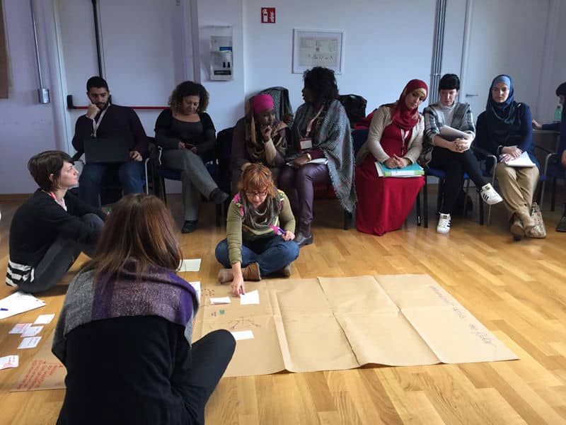 Workshop participants engage in group activity, discussing ideas and writing on large paper sheets.