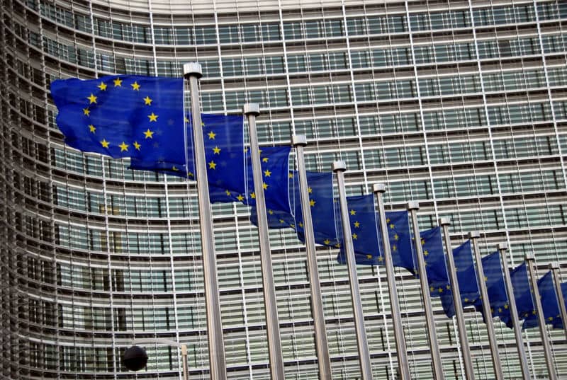 European Union flags waving in front of a modern glass building.
