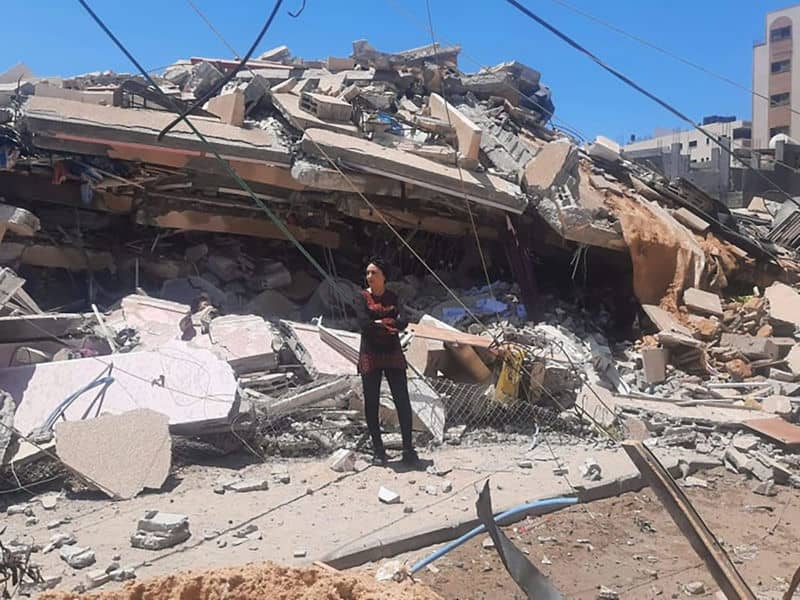 Person stands amidst building rubble under a clear blue sky.