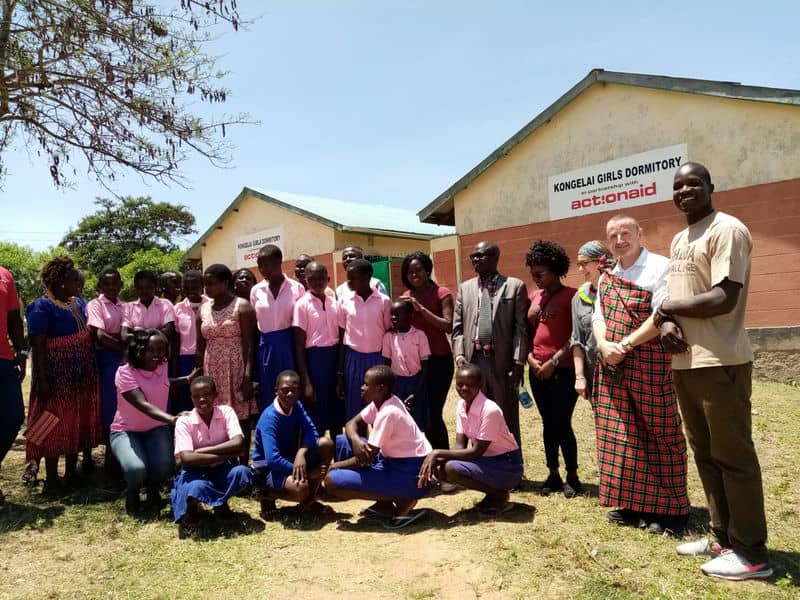 Group photo at Kongelei Girls Dormitory, ActionAid event, featuring students in uniforms and staff outdoors.