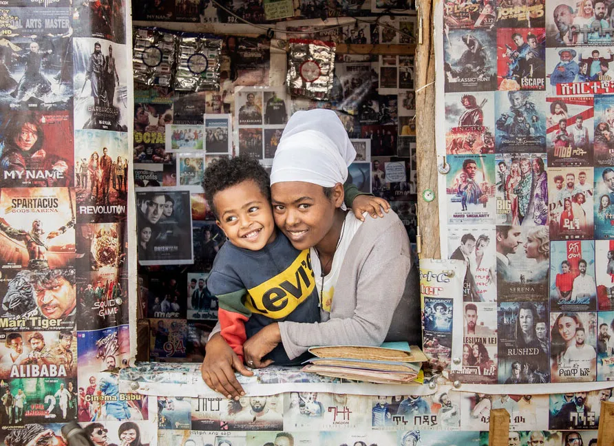 A woman and child smiling at a movie poster-covered counter, conveying joy and community interaction.