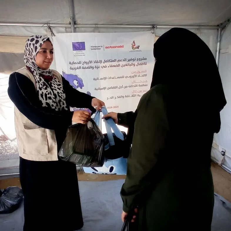 Two women exchange bags at a humanitarian aid event in a tent setting.