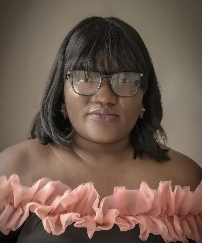 Person wearing glasses and a ruffled off-shoulder top, posing in a neutral setting.