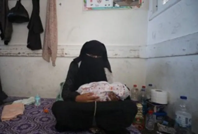 Mother in black niqab gently holding newborn in modest room, surrounded by essentials.
