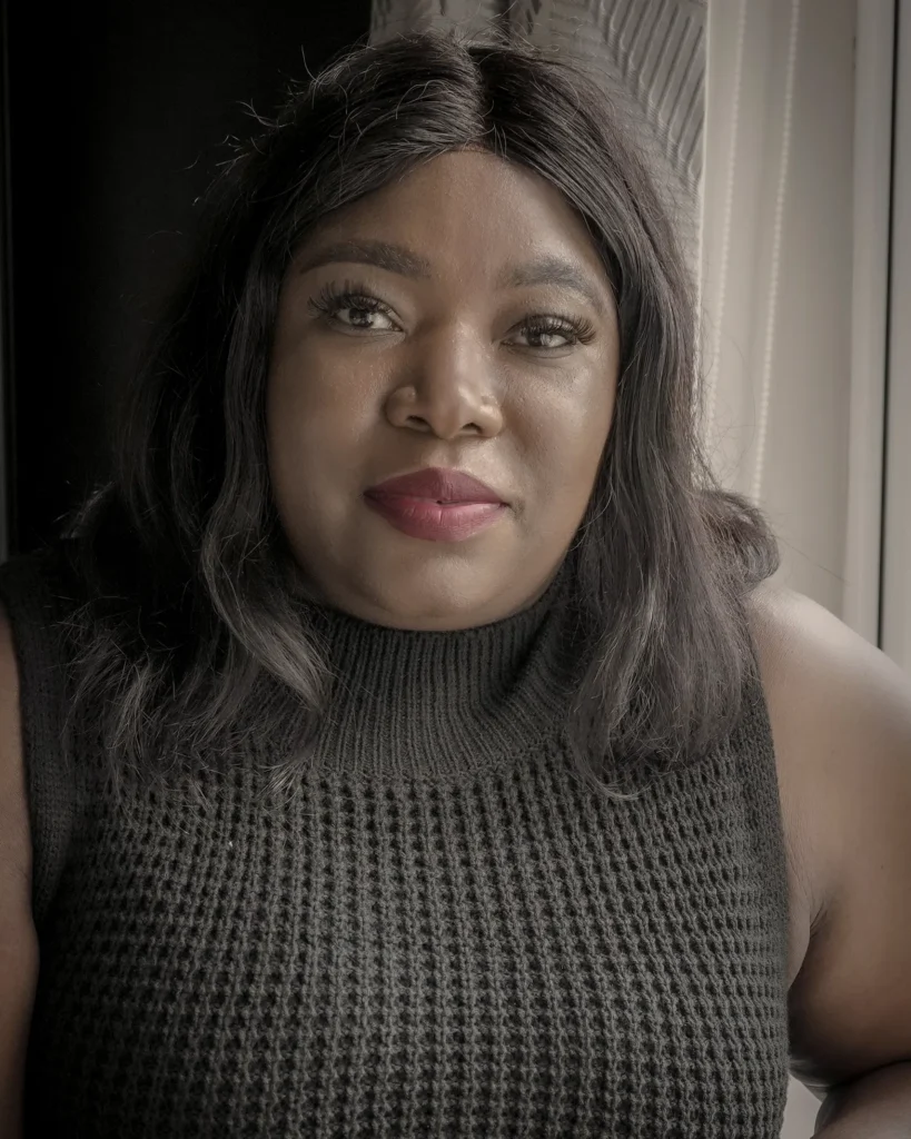 Portrait of a woman in a knitted sweater, sitting by a window with natural light highlighting her face.