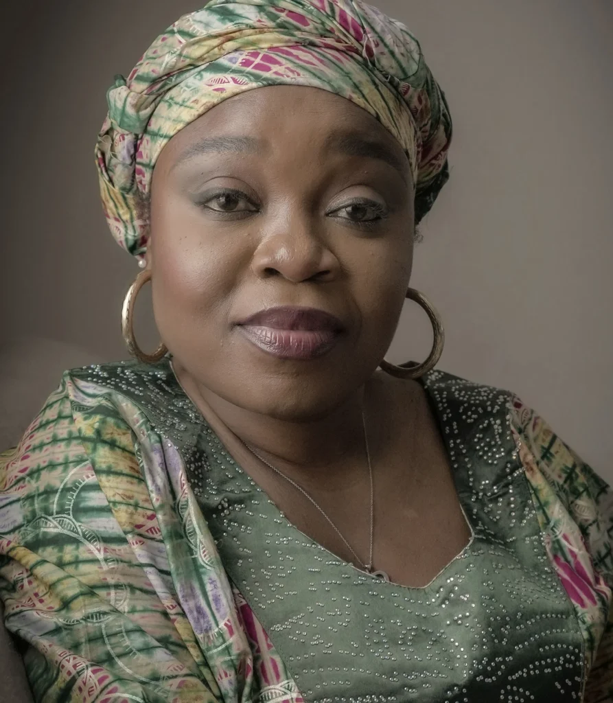 Portrait of a woman in a patterned headscarf and dress, exuding confidence and grace.
