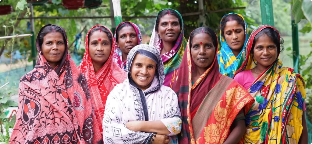 Group of women in colorful sarees smiling outdoors, symbolizing empowerment and community.
